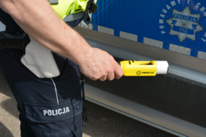 Zbliżenie dłoni policjanta trzymającej alkotest na tle radiowozu