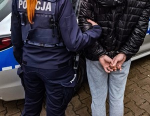 Zbliżenie pleców widzianych z tyłu policjantki i mężczyzny ze skutymi rękami