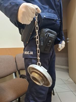 Policjant trzymający w dłoni na łańcuchu dekiel od hydrantu