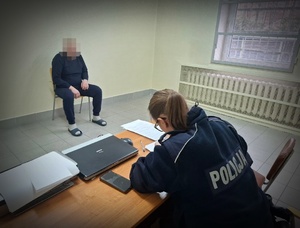 W pomieszczeniu aresztu policjantka sporządzająca dokumentację oraz mężczyzna siedzący na stołku