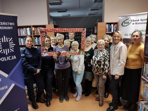Grupa seniorek pozująca do zdjęcia z dwiema policjantkami w bibliotece