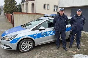 Dwaj policjanci na tle radiowozu i osiedla domów jednorodzinnych
