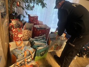 Policjant pochylony nad świątecznymi torbami z prezentami