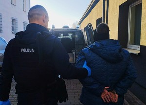 Policjant doprowadzający do radiowozu typu bus mężczyznę