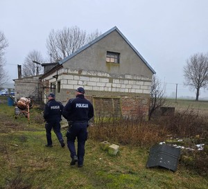 Widziani od tyłu dwaj policjanci na opuszczonej posesji