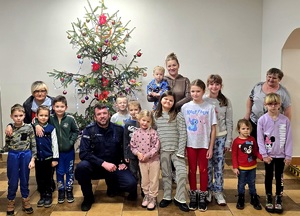 Policjant, wychowawczyni oraz grupa dzieci pozująca do zdjęcia na tle choinki świątecznej
