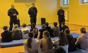 Trójka policjantów w trakcie pogadanki do siedzącej w sali gimnastycznej grupy dzieci.