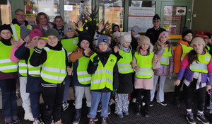Grupa przedszkolaków w kamizelkach odblaskowych pozująca do zdjęcia z wychowawcami oraz policjantką.