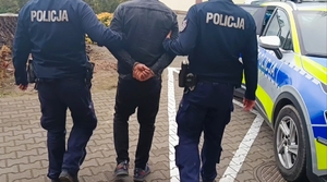 Widziani z tyłu dwaj policjanci prowadzący mężczyznę ze skutymi rękami