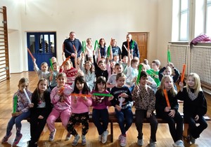 W sali gimnastycznej grupa dzieci pozująca do zdjęcia z dwoma policjantami i wychowawczyniami