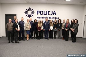 Grupa osób, w tym policjanci pozujący do zdjęcia na tle nazwy jednostki Policji