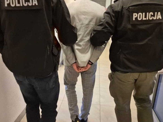 widziani z tyłu dwaj policjanci prowadzący mężczyznę ze skutymi rękami