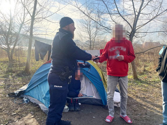 Policjant oraz mężczyzna ubrany po cywilnemu przy namiocie stojącym na ugorze.