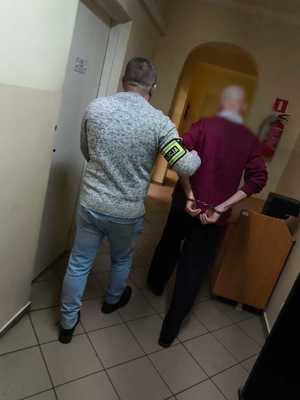 W korytarzu komisariatu policjant prowadzący mężczyznę ze skutymi rękami