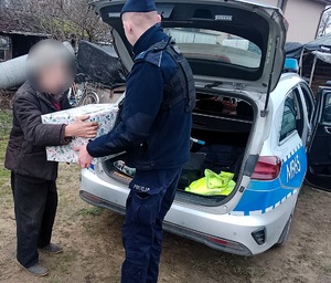 Policjant i starszy mężczyzna odbierający paczkę z bagażnika radiowozu