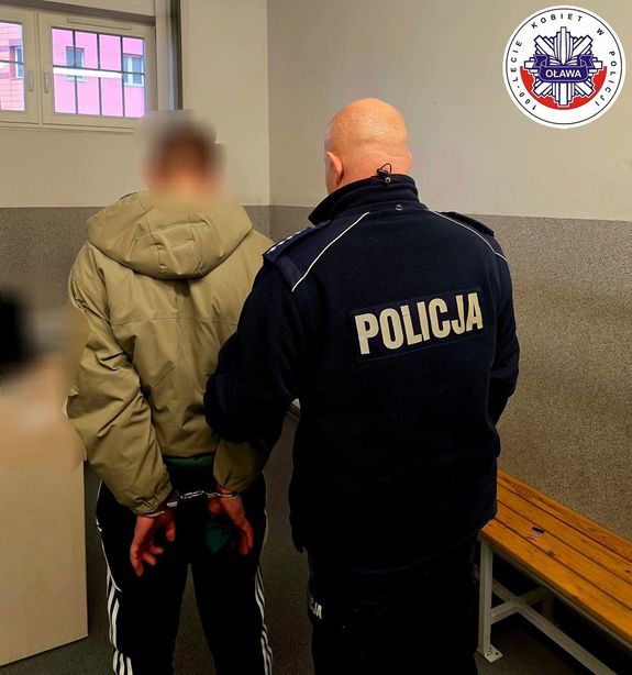 W policyjnej celi widziani z tyłu policjant i mężczyzna w beżowej kurtce