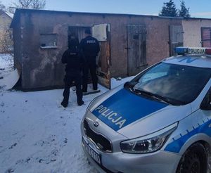 Dwóch policjantów obok starego budynku gospodarczego, z boku radiowóz
