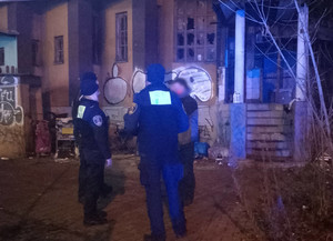 Dwaj policjanci oraz mężczyzna na tle pustostanu w scenerii nocnej