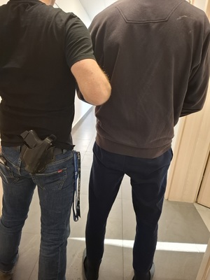 Widziani od tyłu w korytarzu: policjant przytrzymujący mężczyznę