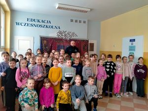 Grupa dzieci pozująca z policjantem do zdjęcia w sali szkolnej