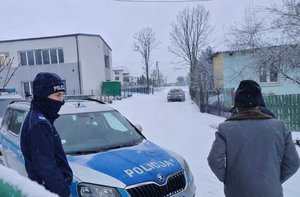 widziani z tyłu w scenerii zimowej obok radiowozu na tle domów jednorodzinnych policjant i starszy mężczyzna