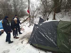 W scenerii zimowych zarośli namiot nakryty folią, a przy nim policjant, strażnik miejski i kobieta po cywilnemu