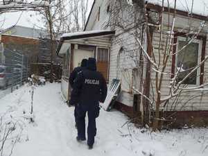 Dwaj policjanci idący do drewnianego budynku w scenerii zimowej