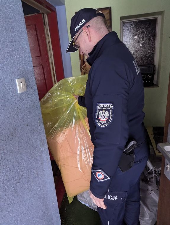 Policjant wewnątrz mieszkania z foliową torbą z kołdrą w rękach