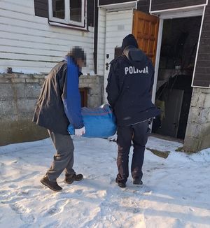 Policjant z mężczyzną niosący worek do piwnicy domu w scenerii zimowej