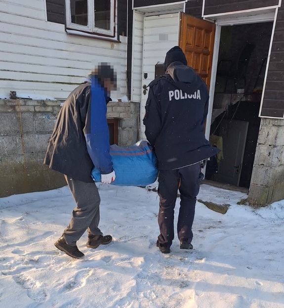 Policjant z mężczyzną niosący worek do piwnicy domu w scenerii zimowej