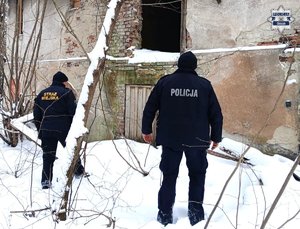 W scenerii zimowej policjant i strażnik miejski na tle pustostanu