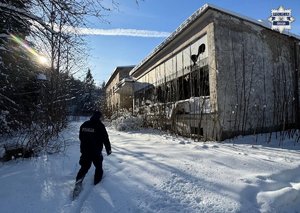 Policjant przedzierający się przez śnieg w kierunku fabrycznego pustostanu