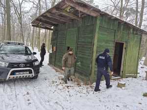 W scenerii zimowego lasu wokół drewnianej szopy policjant oraz dwaj strażnicy leśni