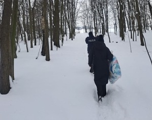 Policjant i kobieta w ciemnej kurtce z torbami w rękach idący ośnieżonym lasem