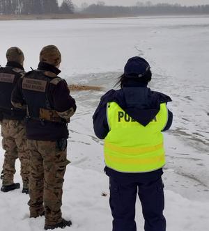 Policjantka oraz dwóch strażników straży rybackiej na ośnieżonym brzegu zbiornika wodnego