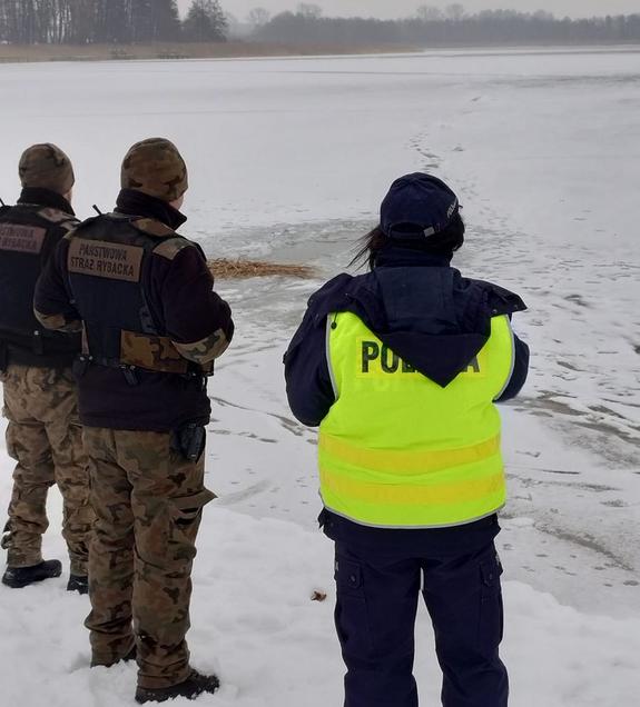 Policjantka oraz dwóch strażników straży rybackiej na ośnieżonym brzegu zbiornika wodnego