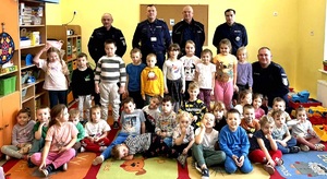 Grupa dzieci w sali szkolnej pozująca do zdjęcia z pięcioma policjantami