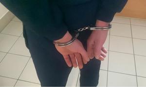 Plecy mężczyzny w ciemnym dresie ze skutymi z tyłu kajdankami rękami