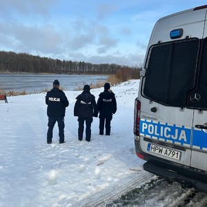 Widziana z tyłu trójka policjantów nad zbiornikiem wodnym w scenerii zimowej