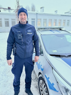 Policjant obok radiowozu na tle ośnieżonego placu