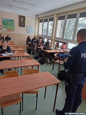 Policjant prowadzący prelekcję dla młodzieży w sali szkolnej