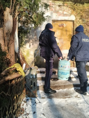 Dwaj policjanci niosący butlę gazową do starego budynku