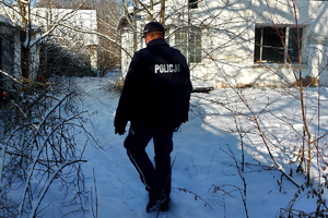 Widziany z tyłu policjant idący w kierunku budynku na ośnieżonej i zaniedbanej posesji