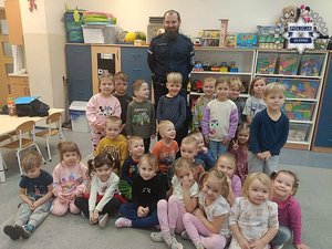 Policjant z grupą dzieci pozujących do zdjęcia w sali przedszkolnej