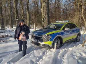 Policjantka w scenerii lasu zimą obok radiowozu z torbami zakupów w rękach