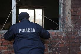 Policjant w scenerii zimowej zaglądający przez otwór okienny do ruiny budynku