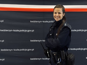 Uśmiechnięta policjantka na tle granatowej ścianki z napisami Kędzierzyn Koźle