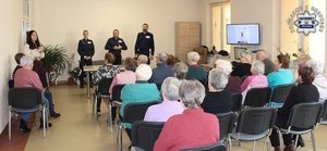 Trójka policjantów prowadząca prelekcję dla seniorów zgromadzonych w świetlicy.