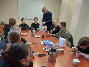 Policjant prowadzący wykład dla młodzieży zgromadzonej przy stole konferencyjnym.