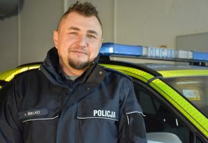 Uśmiechnięty policjant na tle radiowozu stojącego w garażu